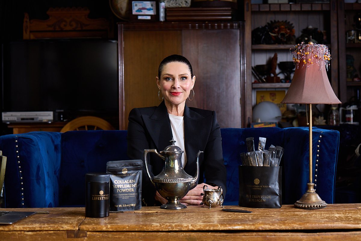 Jacqui Hutton seated at a wooden table with a Collagen Supplement Powder bag, a silver teapot and a black canister